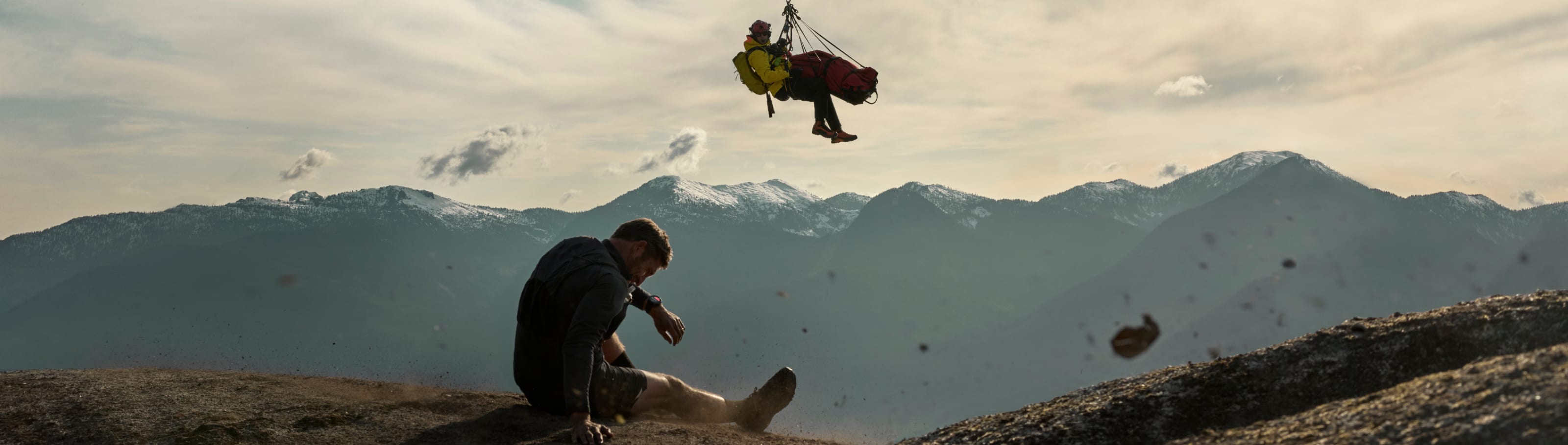 A search and rescue responder being lowered down to help an injured man on a mountain ridge